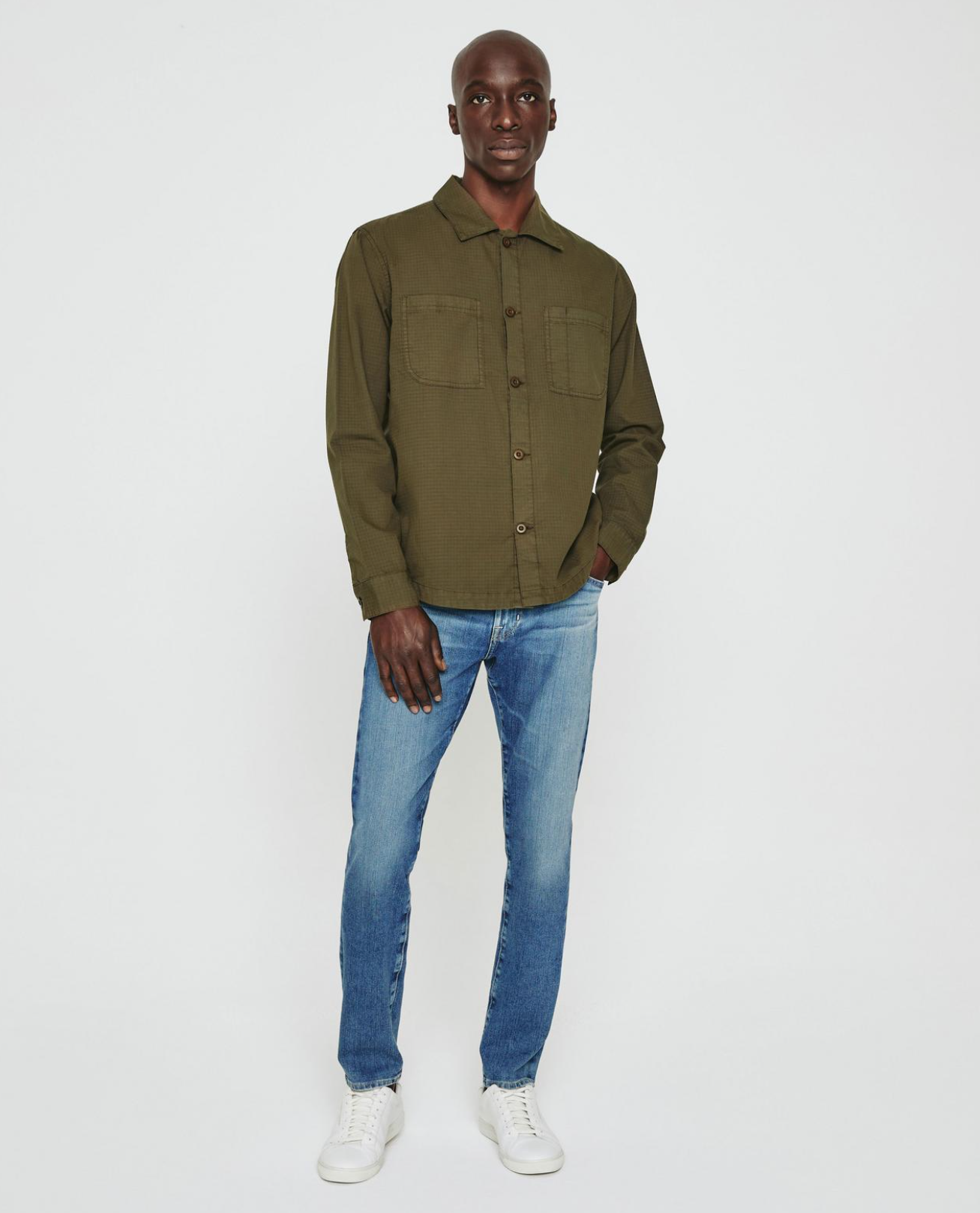 model facing forward wearing ag jeans dylan slim fit jean in talavera blue, paired with an olive shirt jacket and white sneakers