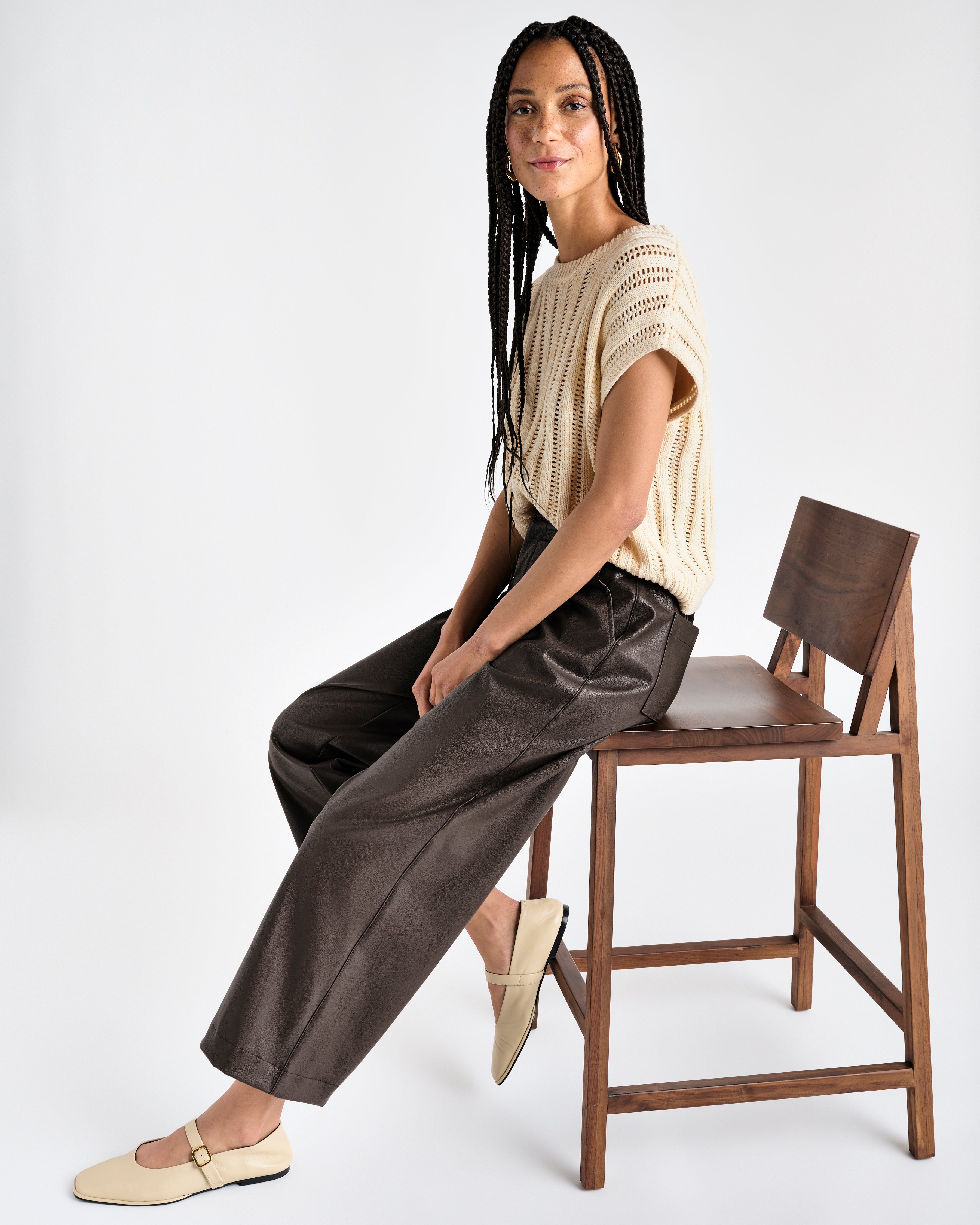 dark brown vegan leather ankle length wide leg trousers, styled with a beige shirt and model is seated