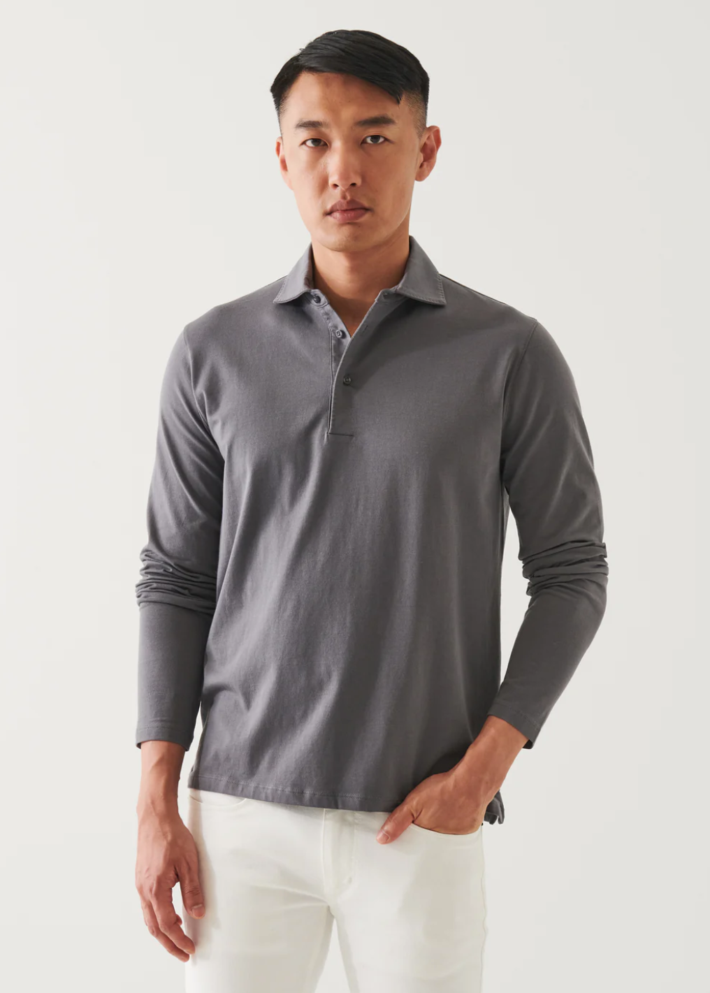 front view of the long sleeve pima stretch polo shirt in light grey, styled with white pants and model's hand in pocket