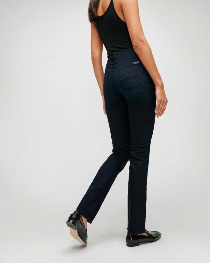 rear view of a model wearing 7 for all mankind's b(air) denim kimmie mid rise straight leg jeans in blue black river thames, a dark blue denim